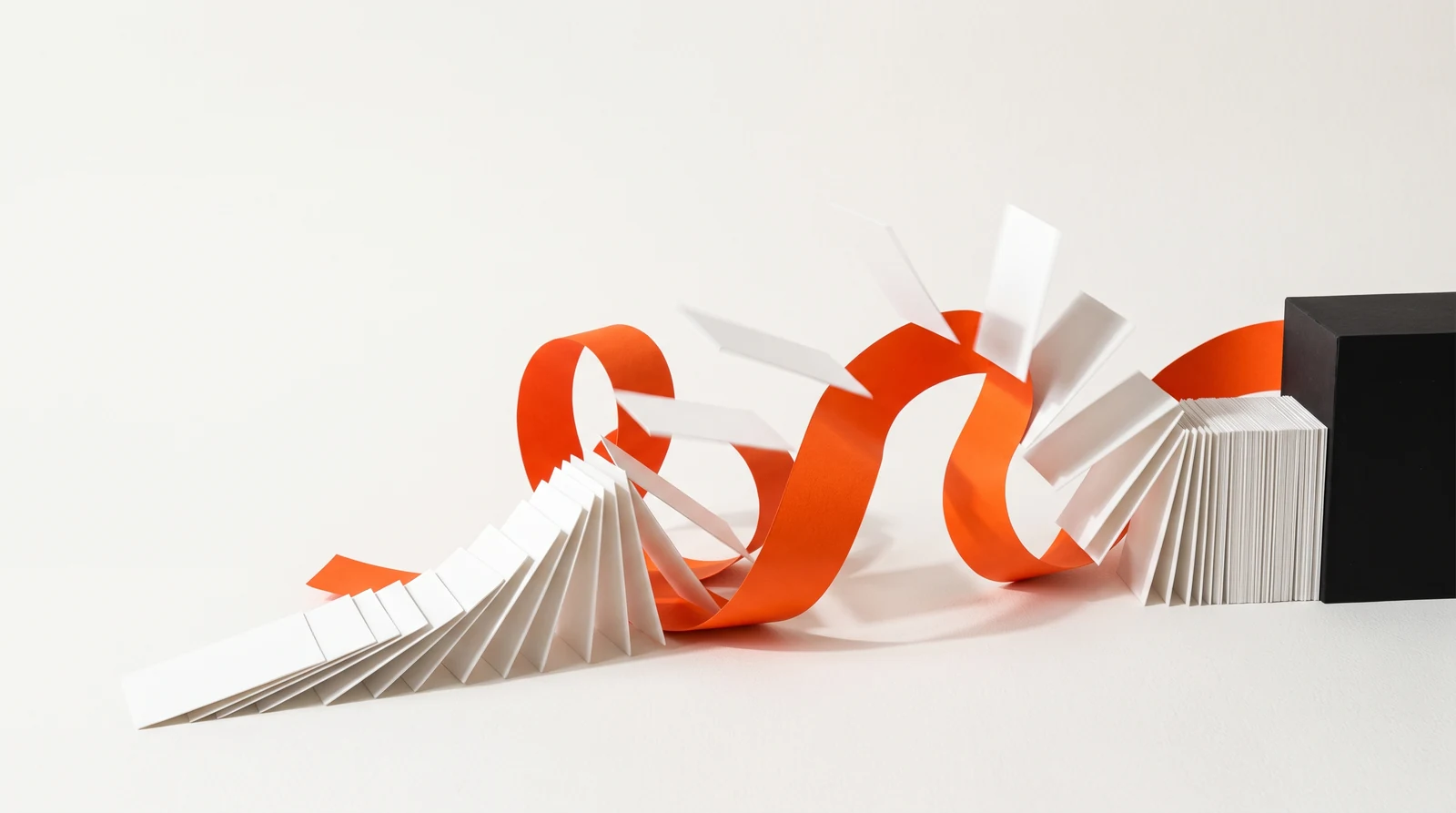 Tarjetas de papel blanco se voltean en ola a lo largo de una cinta naranja y se apilan ordenadamente junto a un bloque negro.